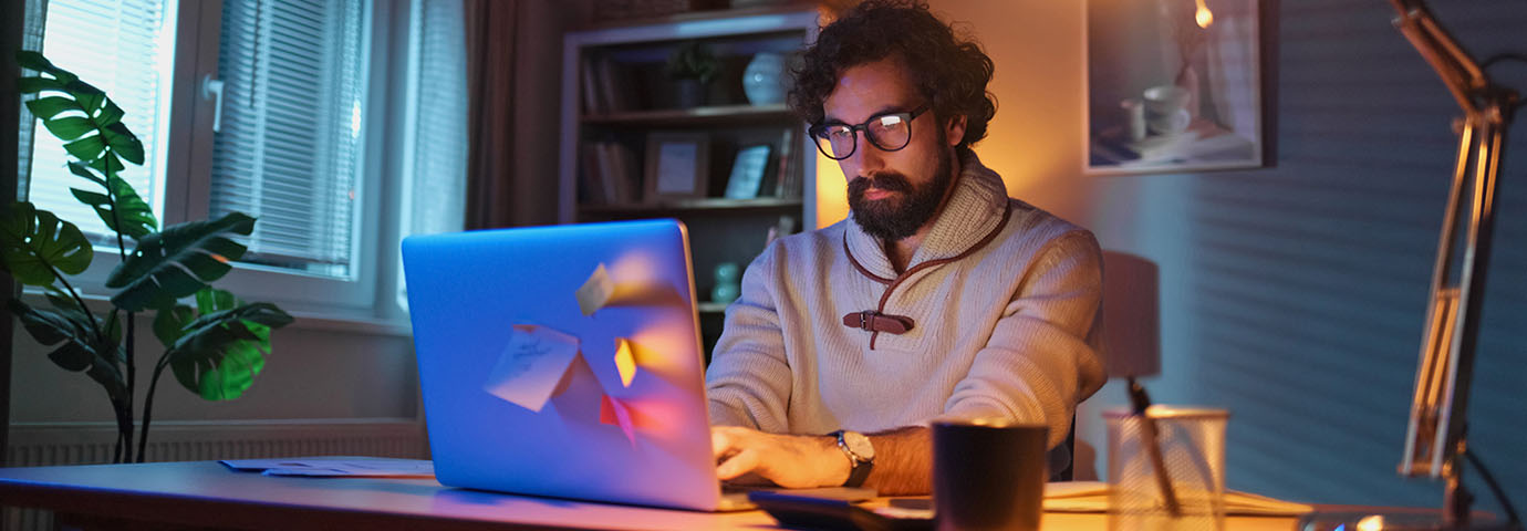 student in dimly lit room at desk working on laptop