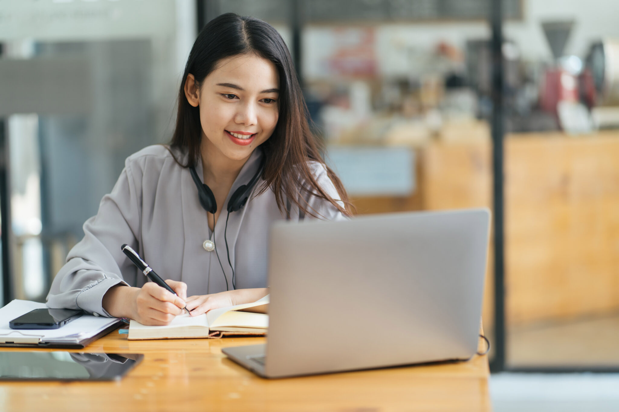 student studying at a desk, writing in a notebook while looking at laptop