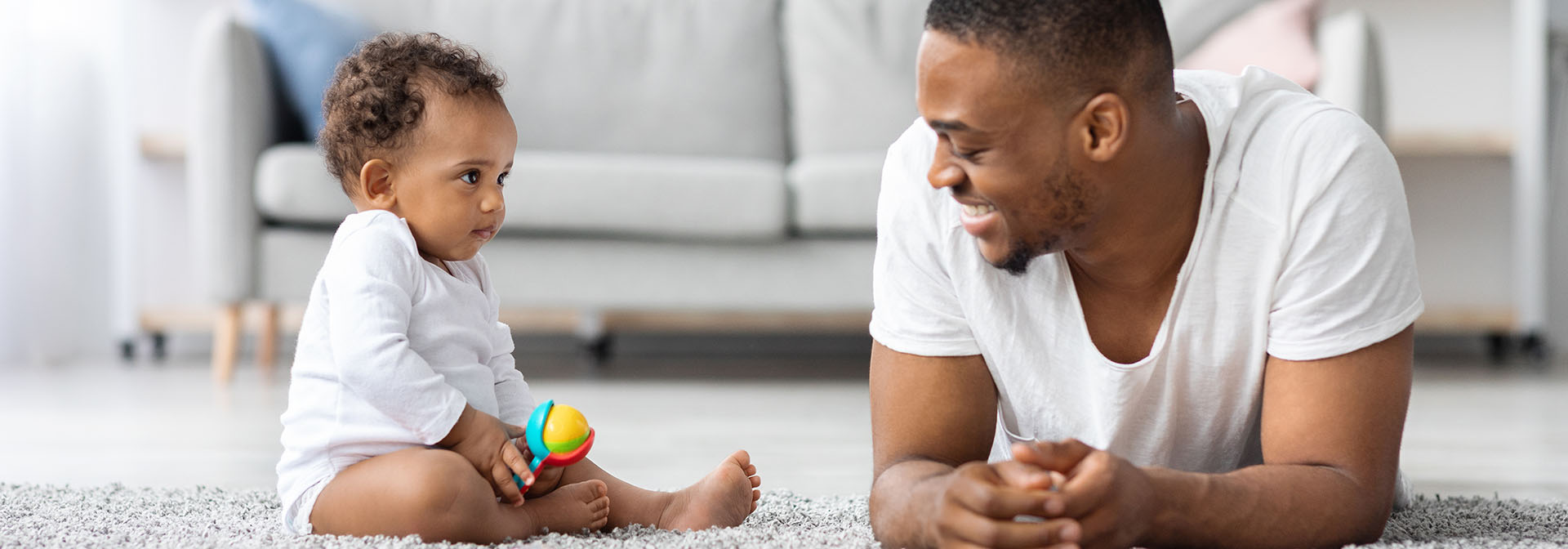 Young happy African American dad playing with cute infant baby sitting up 
