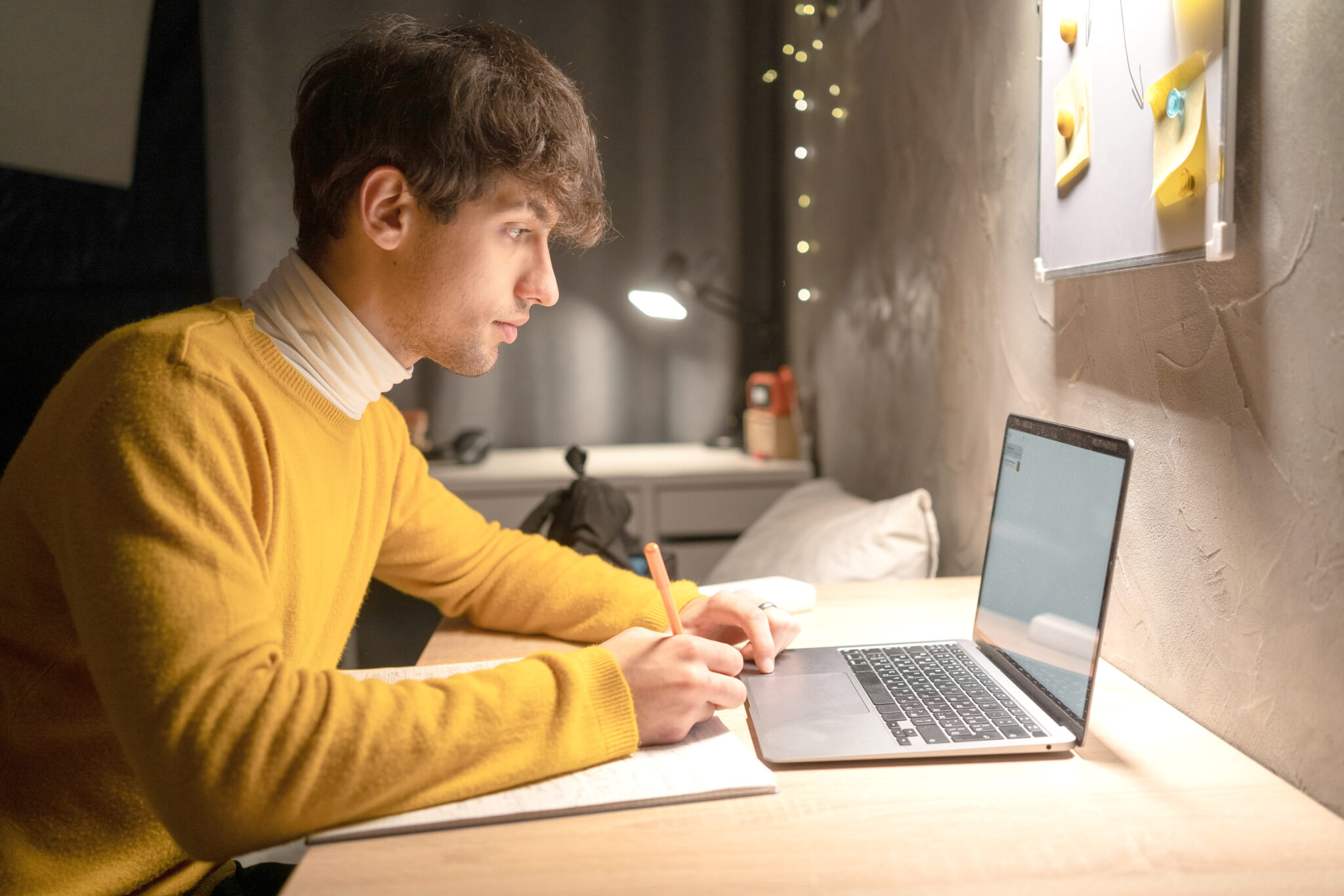 student writing while sitting in front of laptop computer